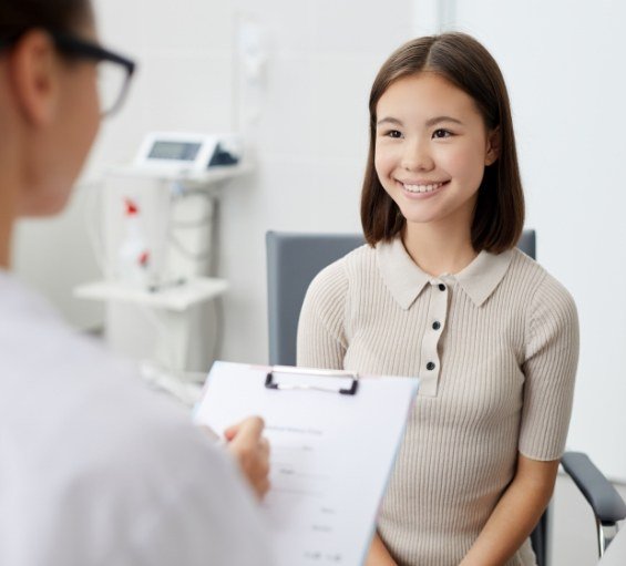 Woman in dental chair smiling as dentist writes on clipboard