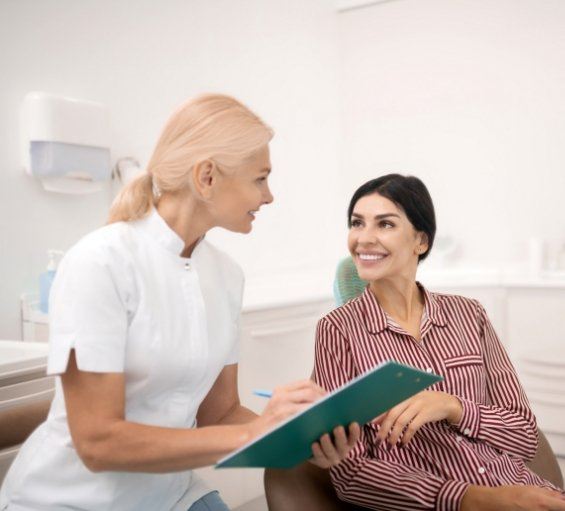 Dental team member with clipboard talking to a patient in the dental chair