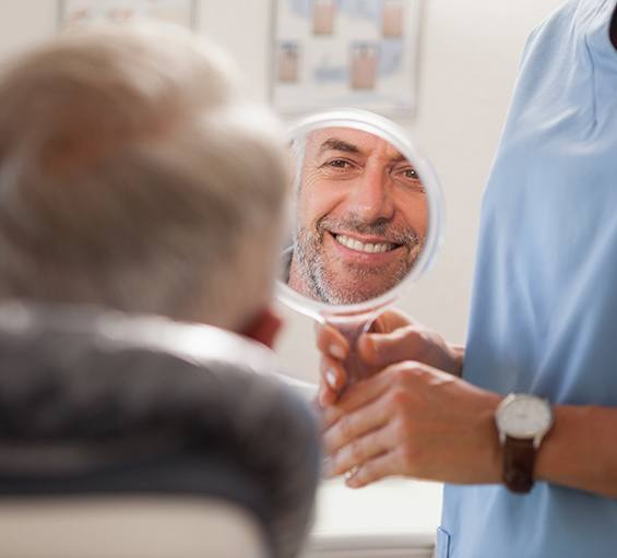 A dentist using a hand mirror to show a patient his smile