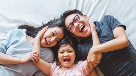 Mother father and young daughter laughing together on bed