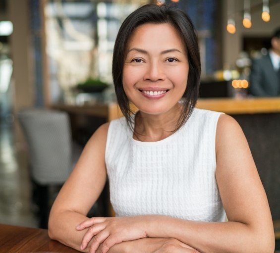 Woman at restaurant table smiling after replacing missing teeth in Windham